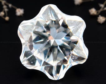 May include: A clear, colorless, faceted gemstone cut into a six-pointed star shape. The stone features numerous triangular and trapezoidal facets that reflect light, creating a bright, sparkling appearance with sharp, defined edges.