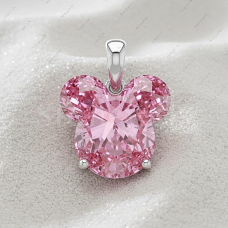 May include: A pink pendant in the shape of a mouse head. The pendant is made of faceted pink gemstones and has a silver bail. The design is a classic and recognizable silhouette, perfect for a necklace.