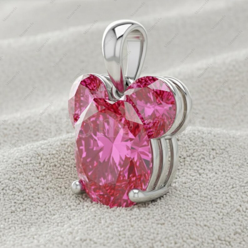 May include: A silver pendant featuring a large, heart-shaped, faceted pink gemstone. The pendant has a loop for a chain and two smaller pink gemstones. The setting is silver, with a polished finish.