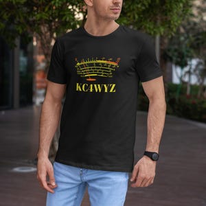 May include: Black t-shirt with a yellow and orange graphic of a radio frequency meter and the call sign KC4WYZ. The shirt is worn with light blue jeans and a black watch.