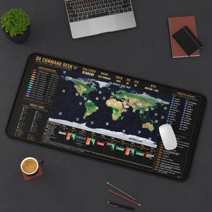 May include: A rectangular desk mat featuring a detailed world map with CQ zones, amateur radio band frequency charts, Morse code reference, and a phonetic alphabet. The black mat includes gold text labels and a colorful map of the continents.