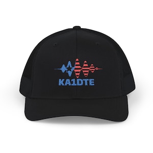 Op de afbeelding: Zwarte truckerpet met een mesh achterkant en een gebogen klep. De voorkant heeft een blauw en rood grafisch ontwerp dat lijkt op een geluidsgolf, met de tekst "KA1DTE" in blauw.