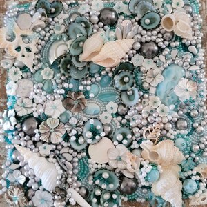 May include: A close-up of a mosaic art piece featuring a variety of seashells, pearls, and other ocean-inspired elements. The piece is made with a variety of materials, including glass, metal, and plastic. The colors are predominantly white, blue, and green.