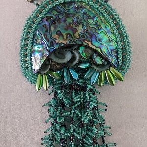 May include: A beaded necklace with a large iridescent abalone shell pendant and a long fringe of green beads.