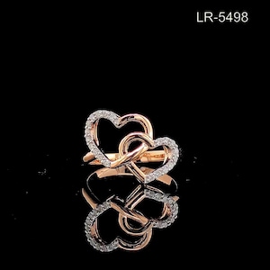 May include: A rose gold ring with two interlocking heart shapes, one set with small diamonds. The ring has a polished finish and a reflective surface, creating a romantic and elegant design.