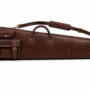 Pode incluir: Um estojo de transporte longo e afunilado em castanho escuro com uma textura de pele de crocodilo. Possui duas pegas superiores, uma alça de ombro ajustável com uma secção almofadada e dois bolsos exteriores com fivelas de cor latão.