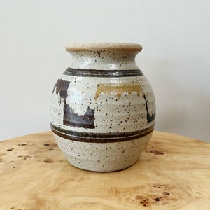 May include: A white ceramic vase with brown and yellow geometric designs. The vase has a speckled glaze and a rounded shape.