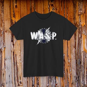 May include: Black t-shirt with the band name "W.A.S.P." in a silver, metallic font. The band's name is set against a stylized, saw-blade design with blue and white accents. The shirt has a crew neck.