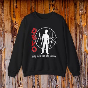 May include: A black long-sleeve sweatshirt featuring a white graphic of a person standing inside a circular atom symbol. The word DEVO is printed in red vertically on the left, and the text duty now for the future is printed in white below.