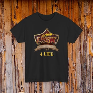 May include: Black t-shirt featuring a gold and burgundy shield design with the text "UGK Underground Kings" and "4 LIFE" in gold lettering. The shirt is made of a soft material and is suitable for casual wear.