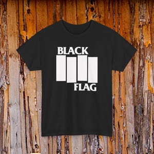 May include: Black t-shirt with the white text "BLACK" above three vertical white bars and the word "FLAG" below. The shirt is made of a soft material and has short sleeves.