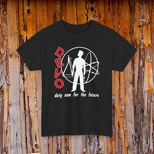 May include: A black short-sleeved t-shirt featuring a white graphic of a person standing inside a circle with scientific symbols. The word DEVO is printed in red vertically, and the text duty now for the future is printed in white below.