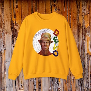 Könnte beinhalten: Ein senfgelbes Sweatshirt mit Rundhalsausschnitt und einem kreisförmigen Aufdruck einer Person mit gemustertem Hut. Der Text "Are We Not Men?" steht in Schreibschrift darüber, und das Wort "DEVO" ist vertikal in bunten Blockbuchstaben abgebildet.