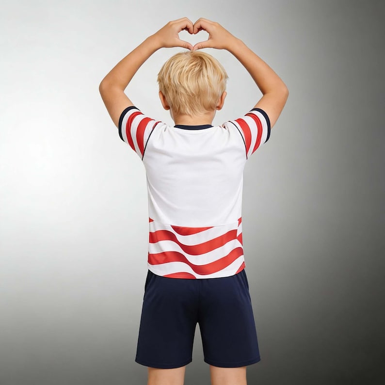 May include: A white and red striped t-shirt and navy blue shorts set. The t-shirt has red stripes on the sleeves and lower portion. The person is making a heart shape with their hands.