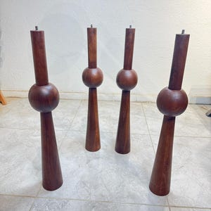 May include: Four wooden furniture legs. Each leg is finished in a dark brown colour, with a rounded midsection and a tapered base. These solid wood legs are designed for furniture.