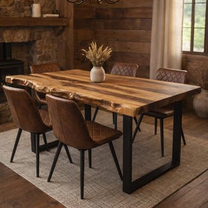 May include: A dining table with a live edge wooden top and black metal legs, accompanied by brown leather chairs. A beige rug is placed under the table and chairs. A chandelier hangs above the table, and a vase with dried flowers is on the table.