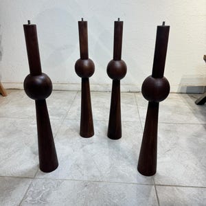 May include: Four dark brown wooden furniture legs. Each leg features a cylindrical top, a spherical mid-section, and a conical base. The legs are displayed on a tiled floor, highlighting their distinctive design and suitability for furniture projects.