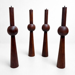 May include: Four dark brown wooden candle holders. Each has a cylindrical top, a spherical middle section, and a conical base. The candle holders are arranged against a white background.
