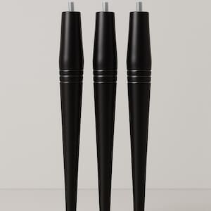 May include: Three black tapered furniture legs with a threaded top for easy attachment. Each leg features two horizontal grooves near the top. The legs are made of a solid, matte black material and are designed for furniture.