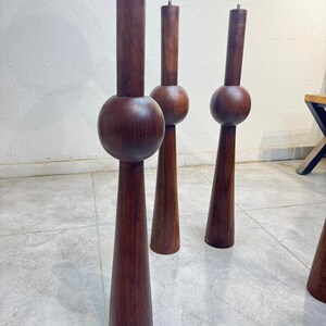 May include: Four dark brown wooden furniture legs. Each leg has a cylindrical top, a spherical middle section, and a conical base. The legs are displayed on a tiled floor, suggesting a mid-century modern design, with a height of approximately 60 cm.