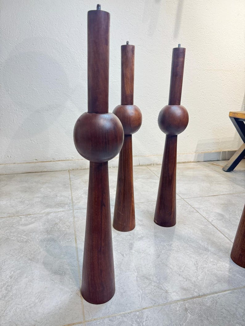 May include: Four dark brown wooden furniture legs. Each leg has a cylindrical top, a spherical middle section, and a conical base. The legs are displayed on a tiled floor, suggesting a mid-century modern design, with a height of approximately 60 cm.