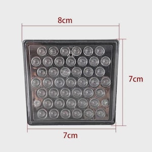 Op de afbeelding: Een vierkant, helder plastic object met 42 kleine, ronde, heldere lampjes. Het object meet 7 cm x 7 cm en is 8 cm breed. De lampjes zijn in een rasterpatroon binnen het vierkante frame gerangschikt.