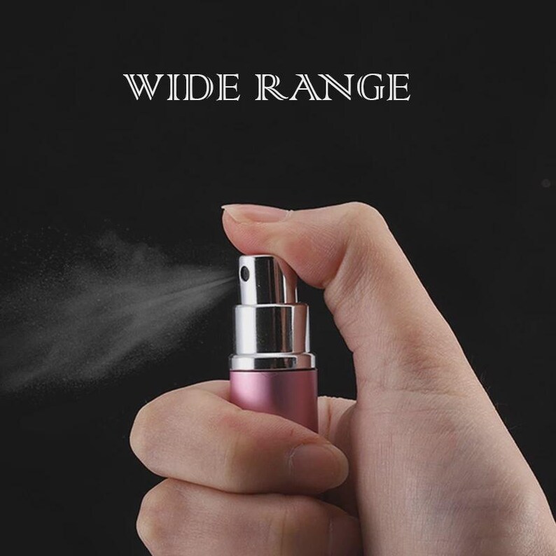 Puede incluir: Un atomizador de perfume rosa y plateado rociando una fina niebla. Las palabras "WIDE RANGE" se muestran en texto blanco en la parte superior de la imagen. El atomizador se sostiene en una mano sobre un fondo negro.
