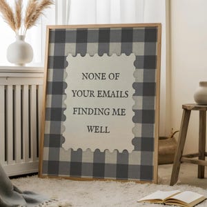 May include: A framed wall art piece with a gray and white checkered pattern and the text "NONE OF YOUR EMAILS FINDING ME WELL". The artwork is displayed in a room with a neutral color palette, a white vase, and a wooden stool.
