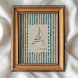 May include: A framed print featuring a sailboat illustration within a postage stamp design. The background has blue and white vertical stripes. The frame is a warm gold color. The text "into the blue" is below the sailboat.