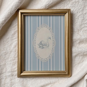 May include: A gold-framed picture featuring a swan illustration. The artwork has a blue and white striped background with an oval, lace-like border around the swan. The swan is depicted in a serene pose, adding a touch of elegance.