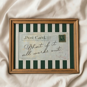 May include: A framed postcard with the text "What if it all works out" in elegant script. The postcard is set against a green and white striped background within a wooden frame, featuring a vintage postage stamp.