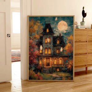 May include: A rectangular wall art print in a light wood frame depicting a multi-story Victorian house at night. The scene features a large full moon, glowing yellow windows, and several white ghost figures floating around the dark blue exterior.