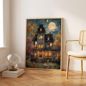 May include: A framed wall art print depicting a multi-story Victorian house at night with glowing yellow windows, several white ghost figures, and a large full moon in the dark blue sky, surrounded by autumn trees with orange and yellow foliage.