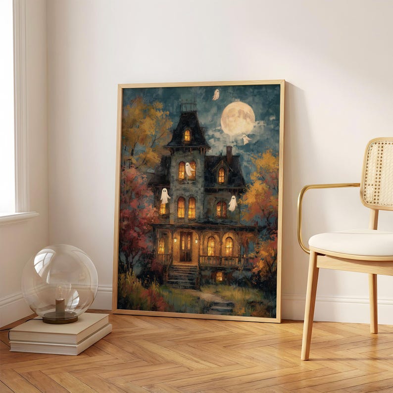 May include: A framed wall art print depicting a multi-story Victorian house at night with glowing yellow windows, several white ghost figures, and a large full moon in the dark blue sky, surrounded by autumn trees with orange and yellow foliage.