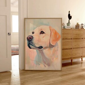 May include: A framed watercolor painting of a yellow Labrador Retriever dog. The dog's head is turned to the side, with a pink nose and light brown eyes. The background has soft pastel colors of pink, blue, and yellow.