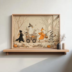 May include: A framed wall art print featuring a whimsical autumn scene with a black cat, a ghost in a witch hat, a fox in an orange coat, and a child in a striped costume pulling a wooden wagon filled with pumpkins through a forest.