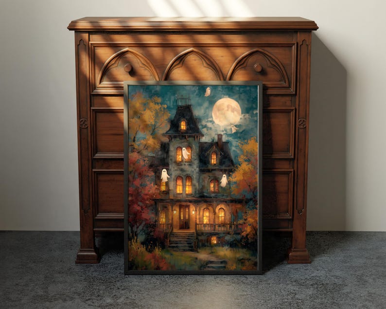 May include: A framed wall art print depicting a multi-story house at night with glowing yellow windows, surrounded by autumn trees in shades of orange and yellow, under a large full moon with several small white ghost figures floating nearby.