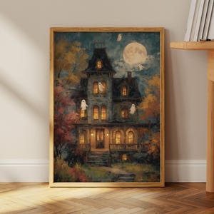 May include: A framed rectangular wall art print depicting a multi-story dark house at night with glowing yellow windows, a large full moon in the sky, and several small white ghost figures floating around the exterior of the building.