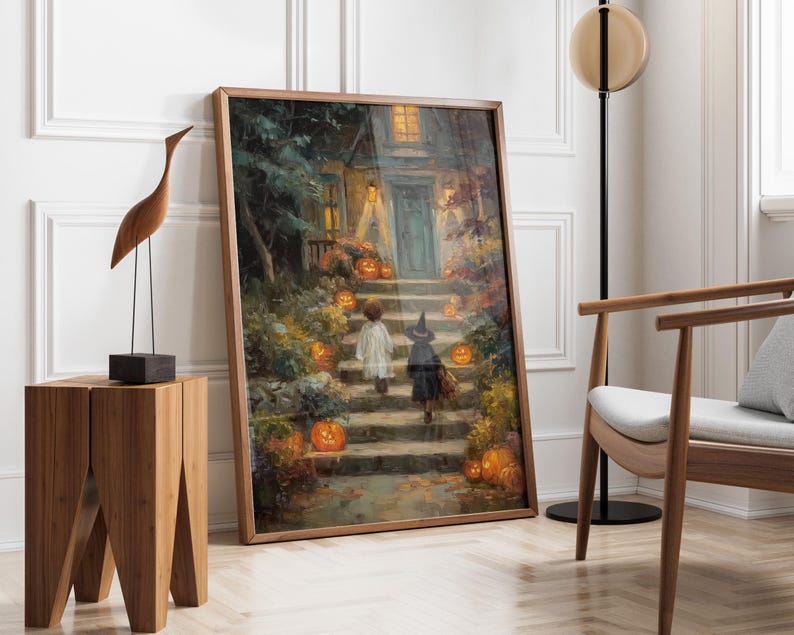 May include: A framed rectangular wall art print depicting a nighttime scene of two children in costumes walking up stone steps toward a house illuminated by warm glowing jack-o'-lanterns and porch lights, surrounded by autumn foliage and trees.