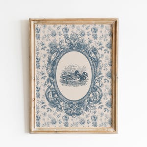 May include: A framed wall art print featuring a central oval medallion with a blue ink illustration of two ducks in a marsh. The background displays a repeating blue floral pattern on a cream-colored surface, enclosed in a wooden frame.