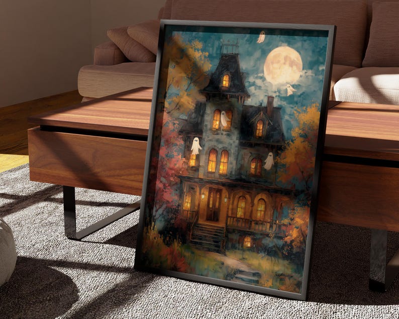 May include: A framed rectangular wall art print featuring a multi-story house with glowing yellow windows, surrounded by autumn trees in shades of orange and red. A large full moon shines in the dark blue sky, with several white ghost figures.