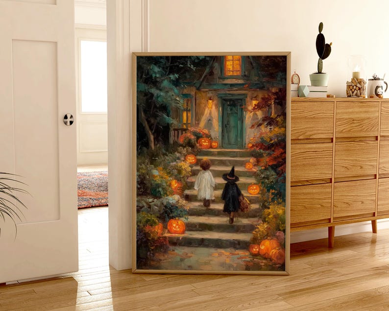May include: A framed wall art print depicting a nighttime scene of two children in costumes walking up stone steps toward a house entrance. The path is lined with glowing orange pumpkins, lush foliage, and warm light emanating from the home windows.
