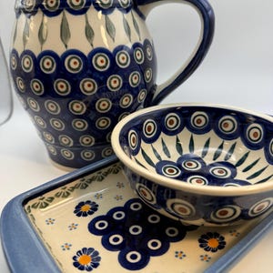 May include: A ceramic pitcher, bowl, and rectangular dish set. The pieces feature a blue and white floral pattern with a repeating design of blue circles with brown and green centers. The pitcher has a large handle.