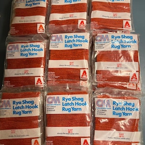 May include: Nine individual clear plastic packages of Columbia-Minerva Rya Shag Latch Hook Rug Yarn in the color Rust 3215. Each package contains 320 pieces of orange yarn, with the brand name and product details printed on the white label.