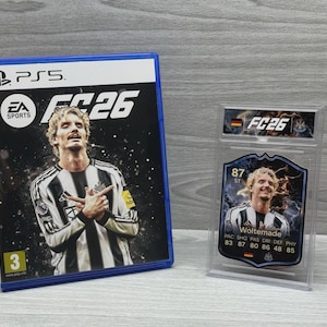 Puede incluir: Una caja de juego de PS5 y una tarjeta coleccionable con un jugador de fútbol. La caja del juego es azul con el texto "FC26" y "EA SPORTS". La tarjeta coleccionable muestra la imagen y las estadísticas del jugador.