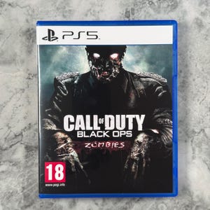Peut inclure: Un boîtier de jeu vidéo PlayStation 5 pour Call of Duty Black Ops Zombies. La couverture présente une silhouette sombre et décomposée en uniforme militaire aux yeux brillants. Le texte Call of Duty Black Ops Zombies est centré avec un logo 18.