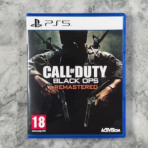 May include: A PlayStation 5 video game case for Call of Duty Black Ops Remastered. The cover features a dark, silhouetted figure holding two handguns with rifles strapped to their back. A red 18 PEGI age rating is visible in the bottom left corner.
