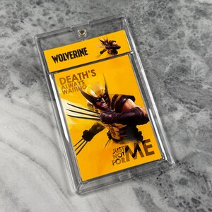 May include: A rectangular trading card featuring Wolverine in a yellow and black suit with extended claws, encased in a clear plastic protective holder. The card has a yellow background with the text Wolverine, Death's Always Waiting, Just Not For Me.