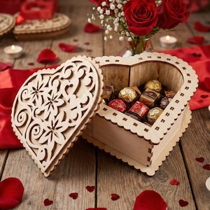Puede incluir: Una caja de madera en forma de corazón con un diseño floral cortado con láser, llena de bombones. La caja está abierta sobre una superficie de madera, junto a pétalos de rosa rojos, velas encendidas y un ramo de rosas rojas. La caja mide aproximadamente 20 cm de ancho.
