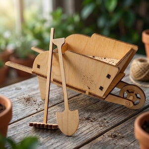 Könnte beinhalten: Eine Miniatur-Holzschubkarre mit einem Schaufel- und Rechenset. Die Schubkarre ist aus hellem Holz gefertigt und hat ein kleines Rad. Schaufel und Rechen sind ebenfalls aus Holz. Das Set ist für die Gartenarbeit konzipiert.